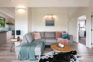 En moderne stue med en grå hjørnesofa, et rundt sofabord og et køkken i baggrunden.