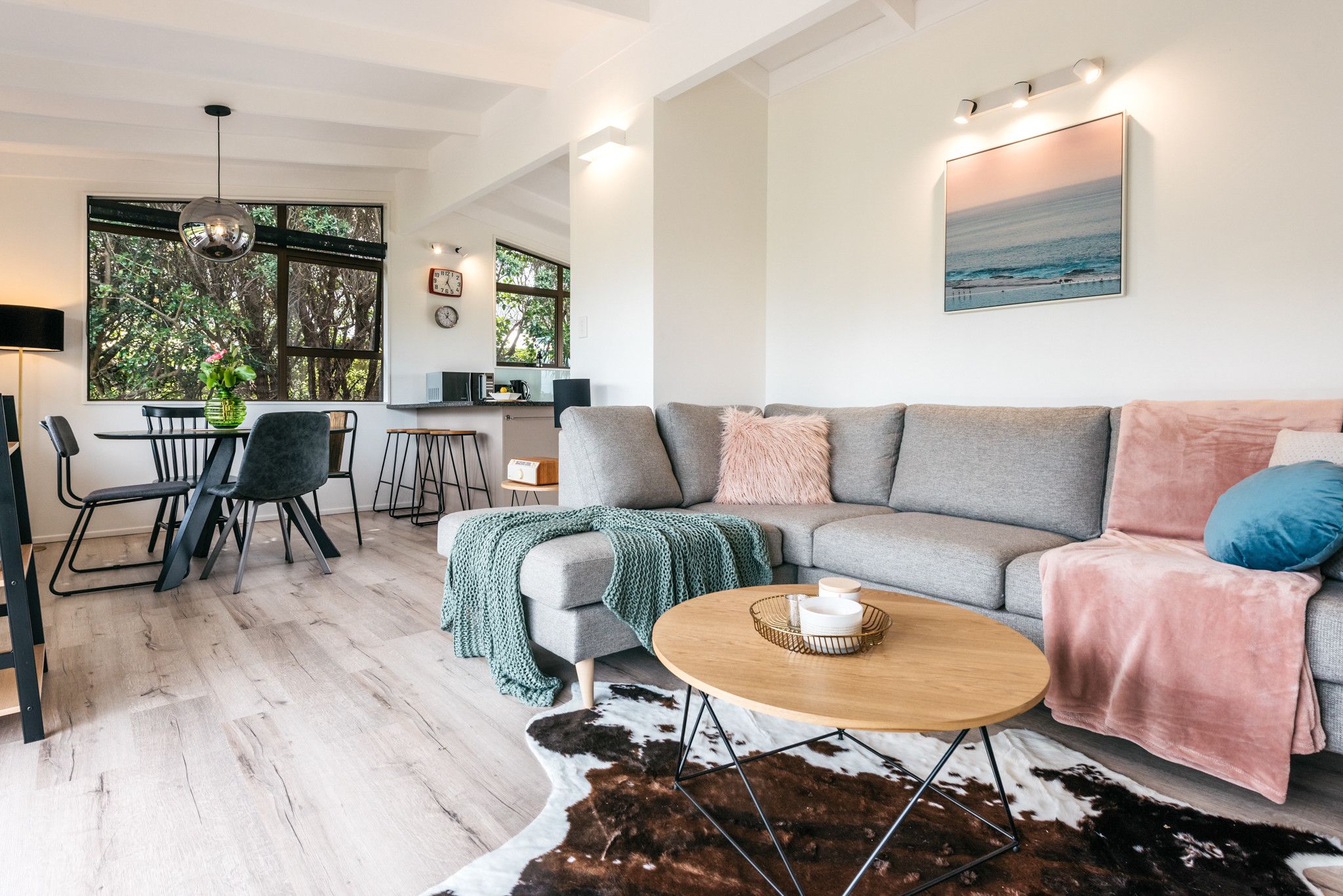 Ein modernes Wohnzimmer mit grauem Sofa, einem Couchtisch und einem Essbereich mit Tisch und Stühlen.