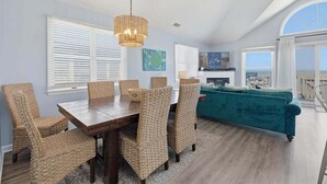 A dining area with wicker chairs, a wooden table, and a hanging light fixture. - Sweet Isabel | Oceanfront | Private Pool, Hot Tub | Nags Head (Nags Head)