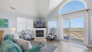 A living room with a sofa, chairs, a fireplace, and a large window with a view. - Sweet Isabel | Oceanfront | Private Pool, Hot Tub | Nags Head (Nags Head)