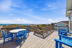 Una terraza de madera con sillas azules y una mesa, con vistas a la playa.