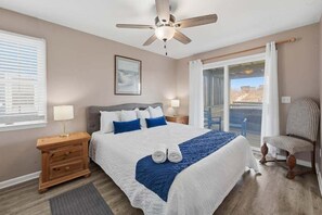 Un dormitorio con cama, ventilador de techo, mesita de noche, una silla y una ventana con persianas.
