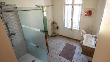 Bathroom features a glass shower enclosure, sink, and window with curtains.