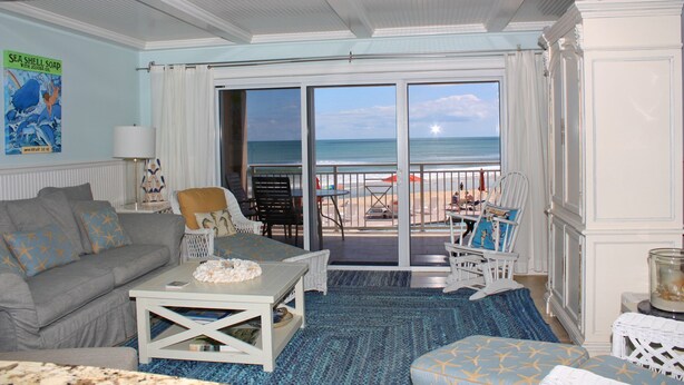 A living room with a view of the ocean, a sofa, a coffee table, and a dining area with chairs. - Beautifully decorated and completely remodeled with custom woodwork throughout... close proximity to geo thermal pools. NO PETS (New Smyrna Beach)