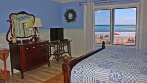 A bedroom with a large bed, dresser, and a television. It features a view of the beach through a large window. - Beautifully decorated and completely remodeled with custom woodwork throughout... close proximity to geo thermal pools. NO PETS (New Smyrna Beach)