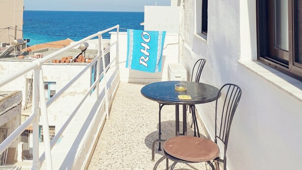 Un balcon avec une table et des chaises, donnant sur une mer bleue et limpide.