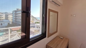 Une chambre dotée d’une grande fenêtre, d’un climatiseur, d’une table de chevet en bois et d’un miroir.