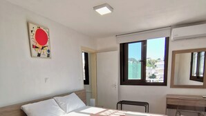 Une chambre à coucher moderne, équipée d’un lit, de tables de chevet, d’un bureau et d’une fenêtre donnant sur un beau paysage.