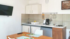 Une cuisine de taille réduite avec des meubles blancs, une table à manger en bois et une seule chaise.