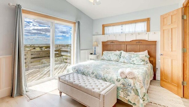 A bedroom with a large window, a ceiling fan, a wooden headboard, and a bench. - Fair Winds | 376 ft from the beach | Private Pool, Hot Tub | Nags Head (Nags Head)