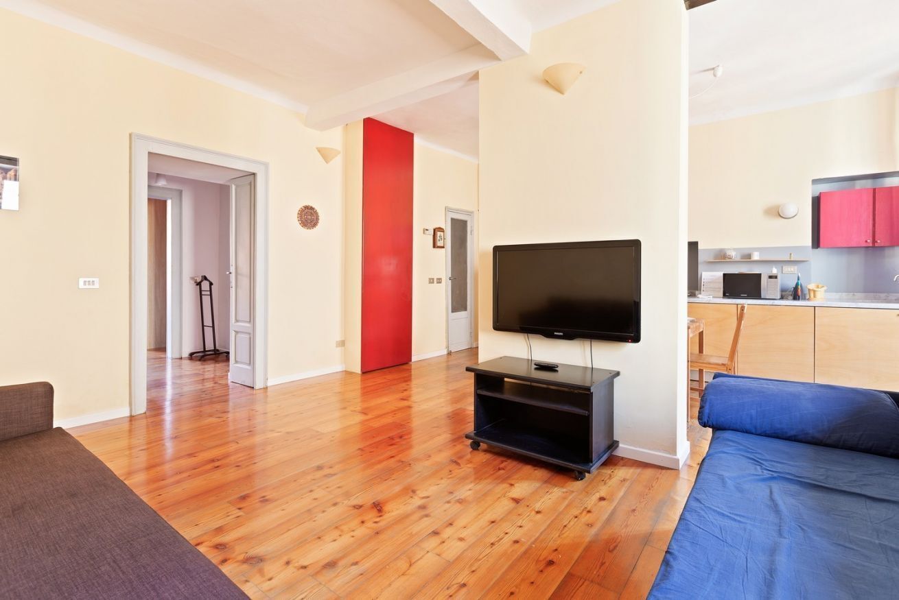 Un soggiorno con TV a schermo piatto, pavimento in legno, un divano blu e una parete di colore rosso.