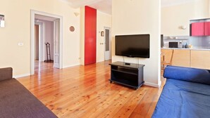 Ein Wohnzimmer mit Flachbildfernseher, Holzboden, einem blauen Sofa und einer Wand in Rot als Gestaltungselement.