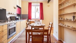 Eine Küche mit Esstisch für vier Personen, Holzschränken, einem eingebauten Backofen und einem Fenster mit roten Vorhängen.