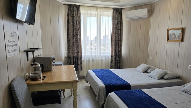 A hotel room with two beds, a desk with a kettle, a chair, a TV, and a window with curtains.