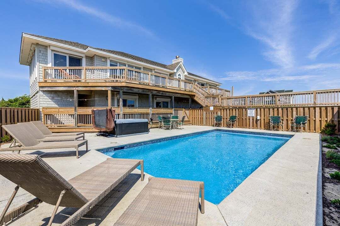 A two-story house with a swimming pool, outdoor furniture, and a wooden deck.