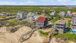 A coastal residential area with houses connected by wooden walkways, a beach, and a clear view of the ocean. - The Porch Life | Oceanfront | Hot Tub | Nags Head (Nags Head)