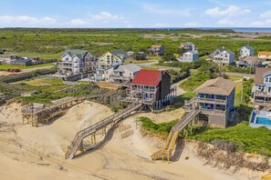 A coastal residential area with houses connected by wooden walkways, a beach, and a clear view of the ocean.