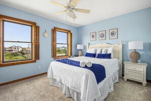A bedroom with a bed, two bedside tables, a ceiling fan, and a window with shutters.