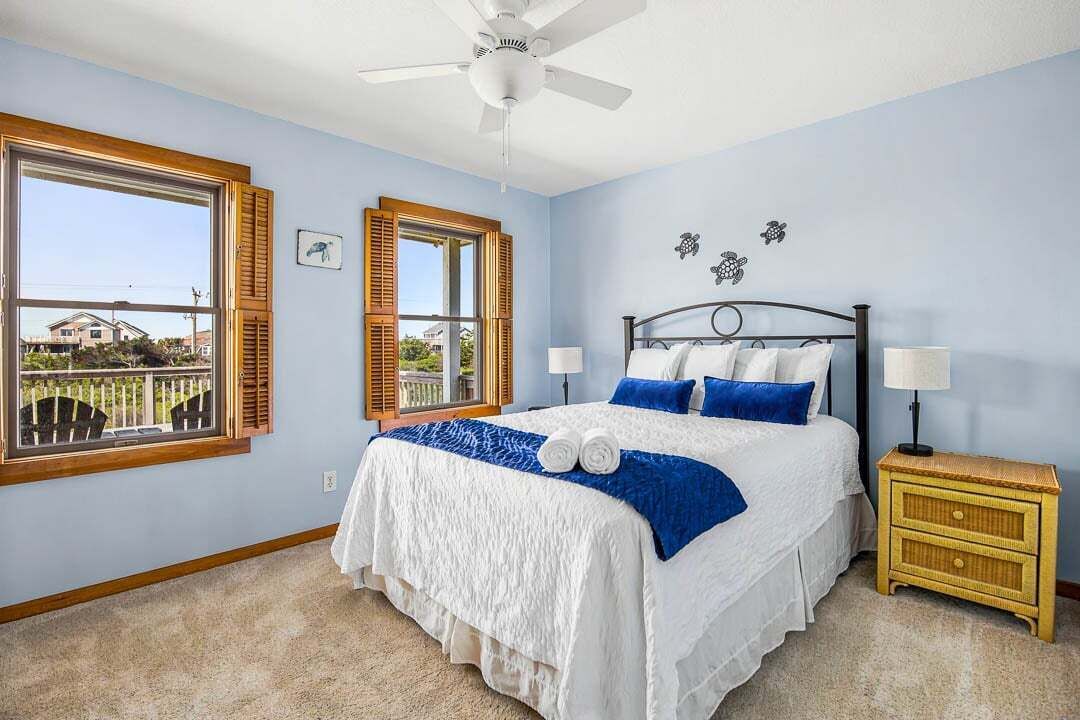 A bedroom with a bed, two bedside tables, a ceiling fan, and a window with shutters.