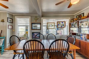 A dining room with a wooden table and chairs, framed artwork on the walls, and a bookshelf with books and decorative items. - The Carriage House I (Upper) | 95 ft from the beach | Dog Friendly, Hot Tub | Nags Head (Nags Head)