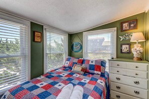 A bedroom with a bed, a dresser, and a window with blinds. - The Carriage House I (Upper) | 95 ft from the beach | Dog Friendly, Hot Tub | Nags Head (Nags Head)