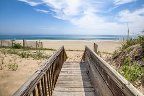 A wooden boardwalk leading to a sandy beach with a clear view of the ocean.