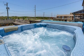 A hot tub with a wooden deck and a view of a beach and buildings in the background. - The Carriage House I (Upper) | 95 ft from the beach | Dog Friendly, Hot Tub | Nags Head (Nags Head)