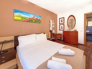 A hotel room with a large bed, a wooden dresser, a desk, and a painting on the wall. - Megan Apartment by Hello Homes Sitges (Sitges)