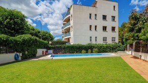 A modern apartment building with a swimming pool, surrounded by well-maintained lawns and hedges. - Megan Apartment by Hello Homes Sitges (Sitges)