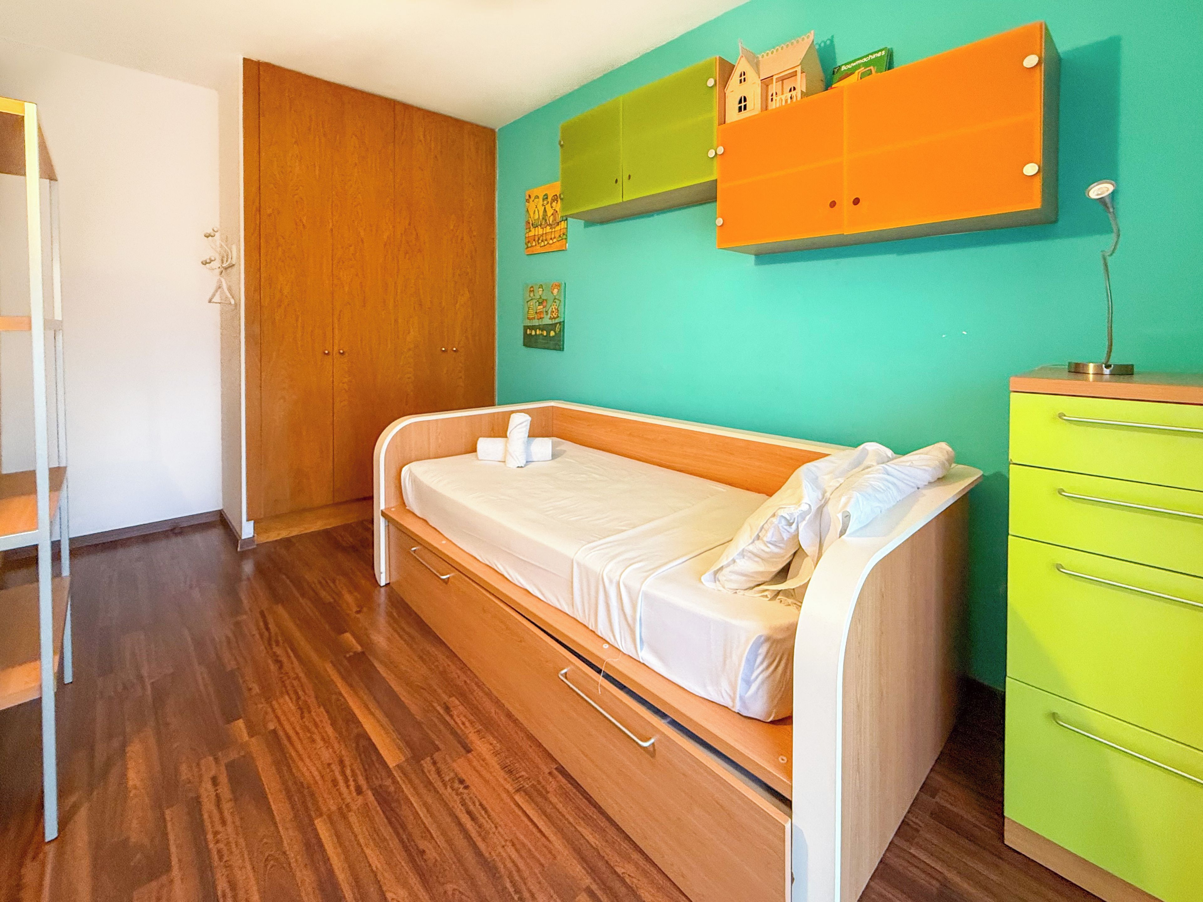 Ein Einzelzimmer mit Holzboden, grüner Wand und Holzschrank.