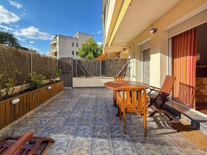 A patio with a wooden table and chairs, a tiled floor, a wooden fence, and a building in the background. - Megan Apartment by Hello Homes Sitges (Sitges)