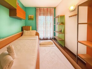 Een hotelkamer met twee bedden, een groene muur, een raam met gordijnen en een plank met een lamp.