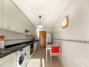 A kitchen with a washing machine, a dining table with chairs, and a refrigerator. - Megan Apartment by Hello Homes Sitges (Sitges)