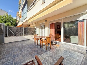 A patio area with a round table and chairs, a sliding glass door leading to a room, and a tiled floor. - Megan Apartment by Hello Homes Sitges (Sitges)