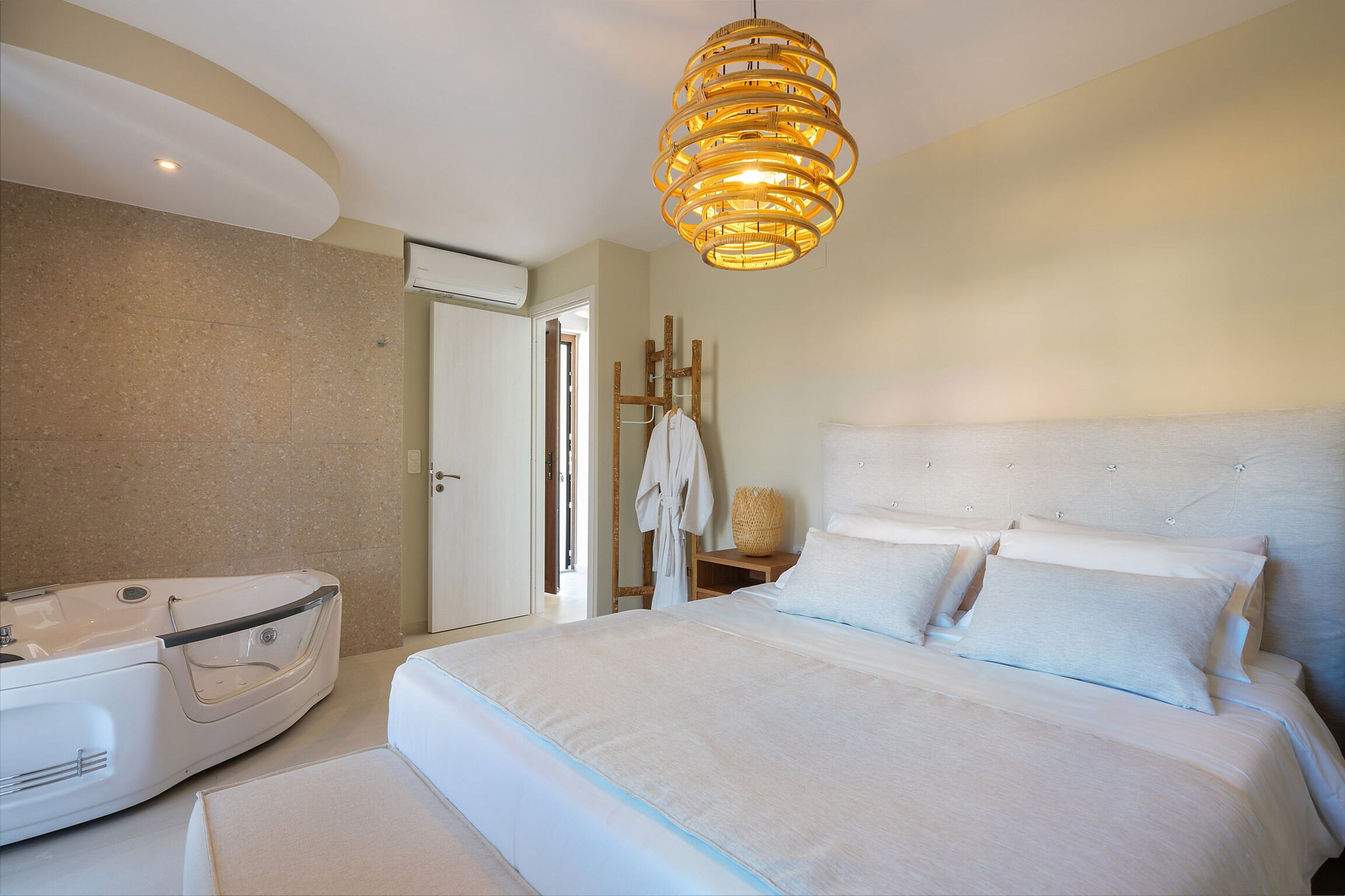 A modern hotel room with a large bed, a white bathtub, and a unique rattan light fixture.