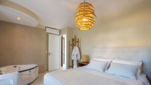 A modern hotel room with a large bed, a white bathtub, and a unique rattan light fixture. - 100m from the beach, kids pool, ping pong, sauna & gym, private sun beds! (Rethymno)