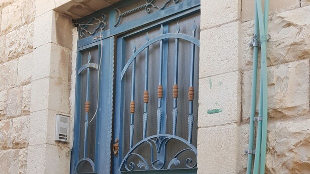 A blue metal gate with decorative elements and a green hose attached to the wall. - Castle House (Al-Karak)