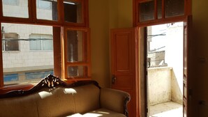 A room with a sofa, a wooden door, and a window with a view of a building outside. - Castle House (Al-Karak)