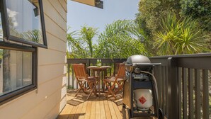 A wooden deck with a barbecue grill and outdoor furniture. - Jacaranda Lodge - Whangamata Upstairs Unit (Whangamata)