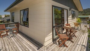 A modern house with a wooden deck, large windows, and outdoor furniture. - Jacaranda Lodge - Whangamata Upstairs Unit (Whangamata)
