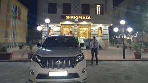 A white SUV parked in front of a hotel with a sign reading "SHARQPLAZA".