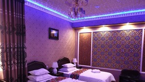 A hotel room with two beds, a chandelier, patterned wallpaper, and a view of the city.