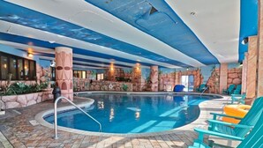 Une piscine intérieure avec un sol carrelé en pierre, un escalier d’accès à la piscine et des chaises longues turquoise.