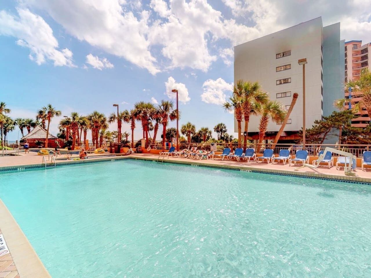 A swimming pool with lounge chairs and palm trees.