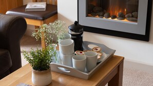 Una bandeja con tazas, una cafetera, una planta en maceta y galletas sobre una mesa de madera.