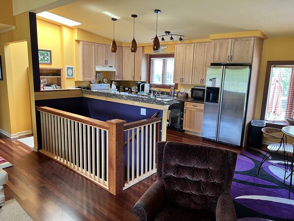 A modern kitchen with wooden cabinets, a central island with a railing, stainless steel appliances, pendant lighting, and a view to the outside. - The Eagle Ranch, central to everything, spacious yet cozy. Quiet setting (Northport)