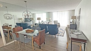 A modern living room with a dining area, blue sofas, and a glass coffee table. - Spectacular OCEAN VIEWS - Fabulous Kingston South Hampton 3rd fl unit (Myrtle Beach)