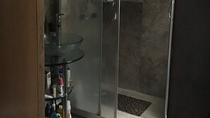A glass-enclosed shower area with a glass door, a towel hanging on the door, and a small shelf with toiletries. - Depa to share in Mexico City (Only Woman) (Roma Sur)