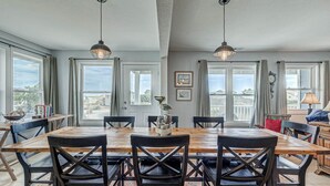 Een eetruimte met een houten tafel en stoelen, grote ramen en hangende hanglampen.