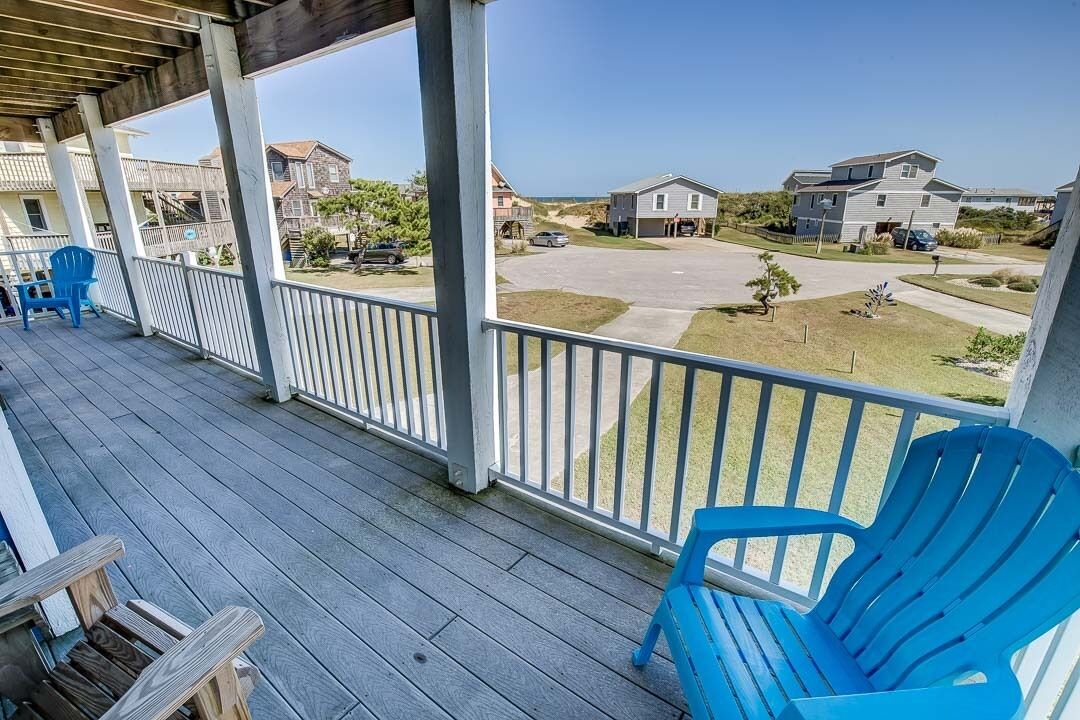 A covered porch with a view of a residential area, including houses and a beach.